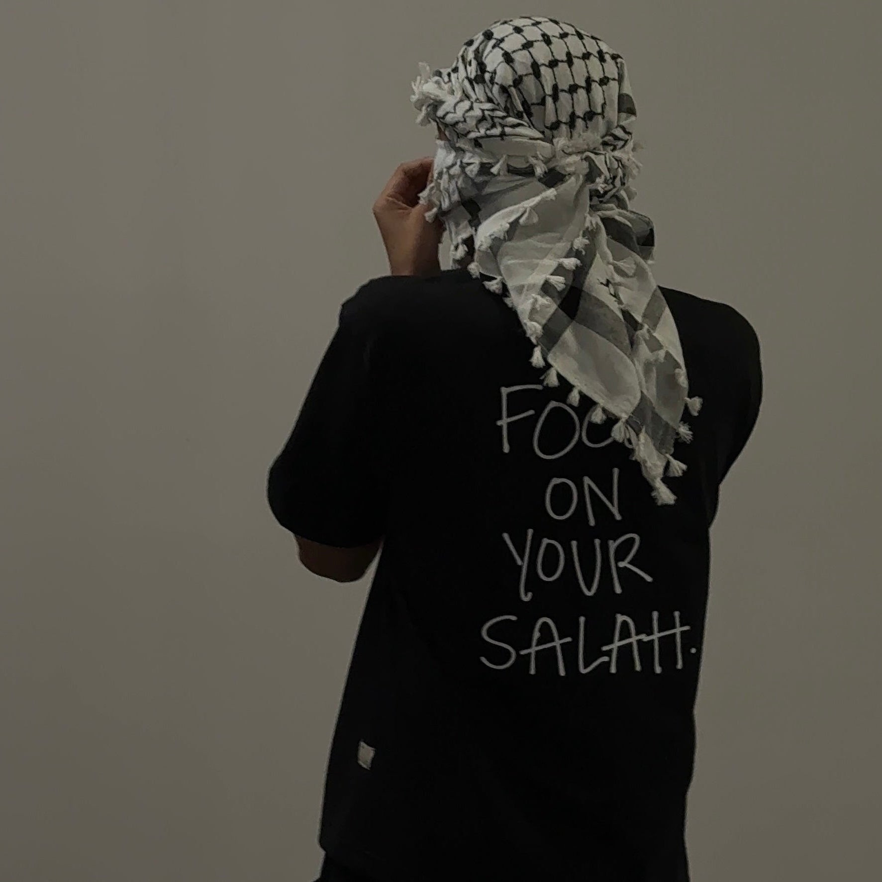 Person wearing a black shirt with 'Focus on Your Salah' text and a white headscarf.