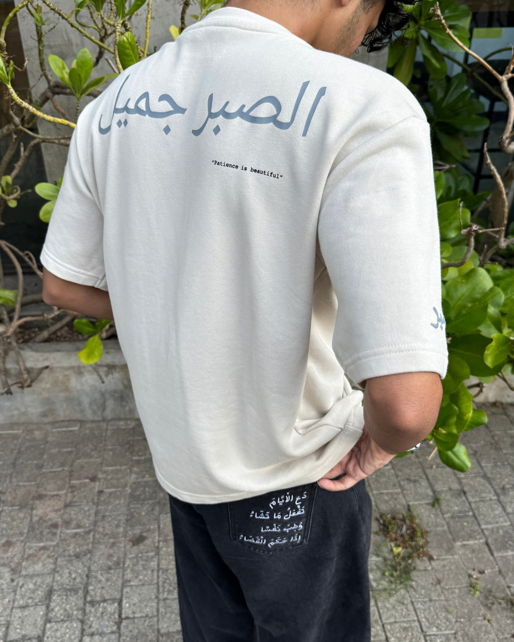 Person wearing a white t-shirt with Arabic text on the back, standing outdoors.