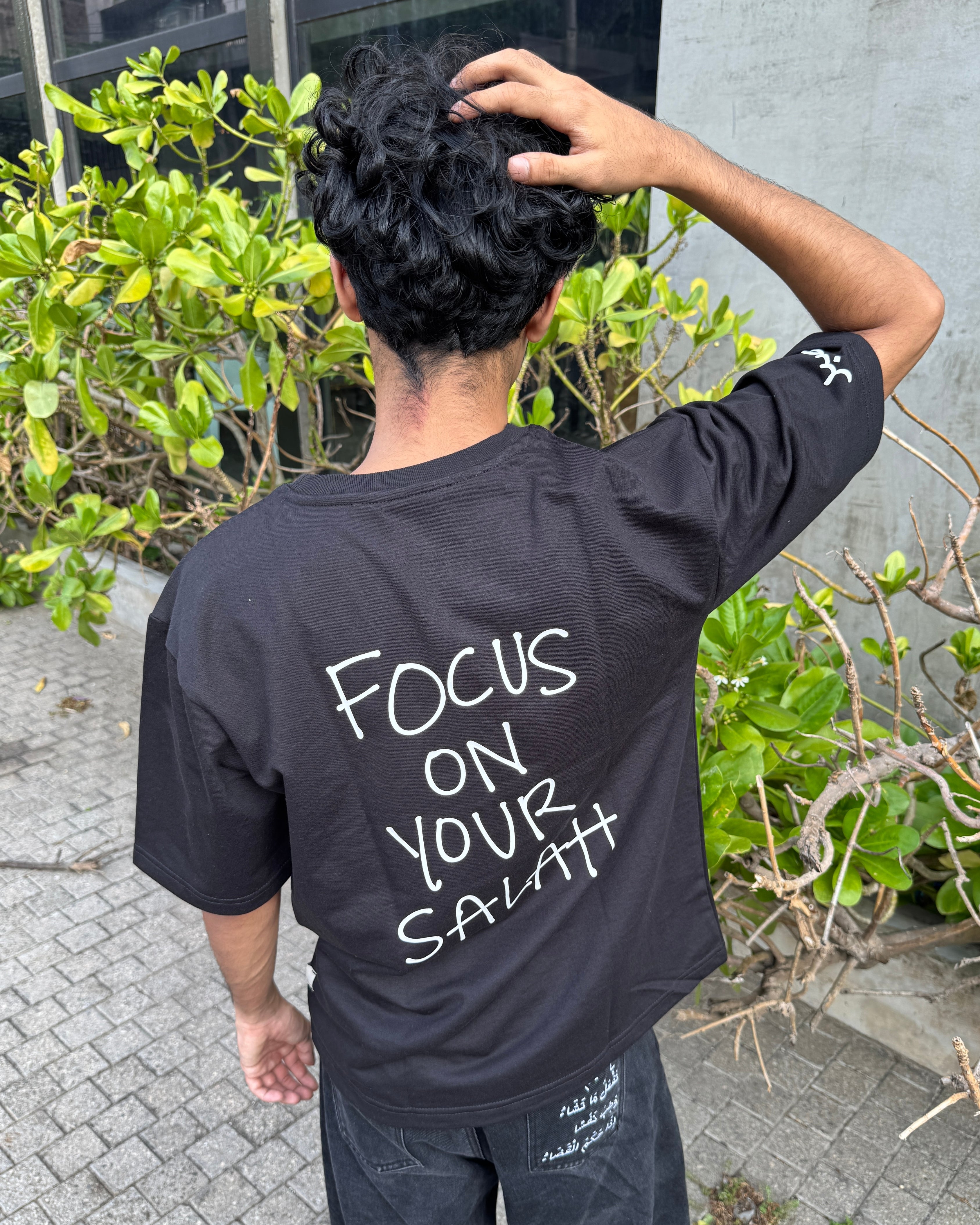 Person wearing a black t-shirt with 'Focus on Your Salat' text outdoors.