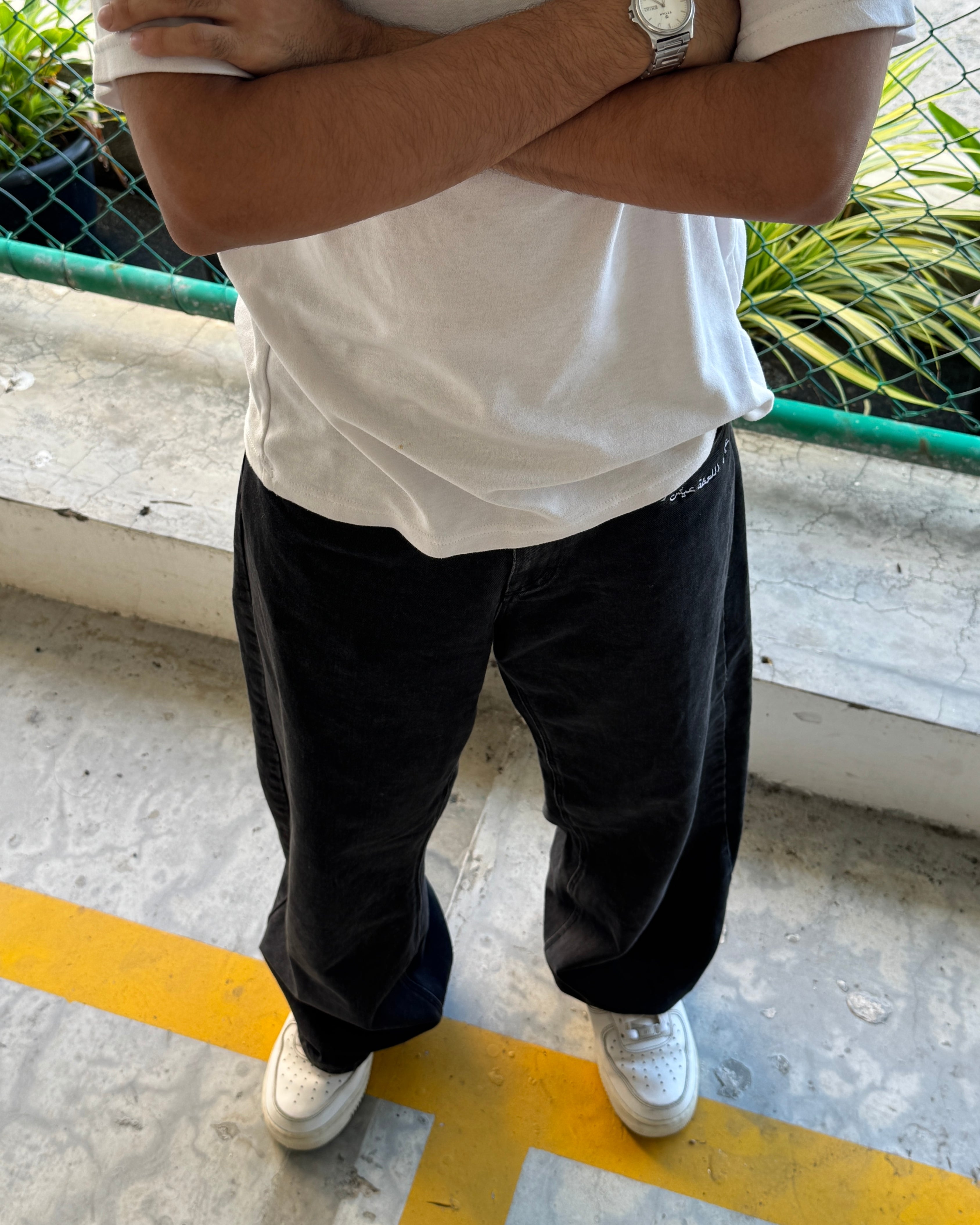 Person wearing a white shirt, black pants, and white sneakers standing on a concrete surface with a yellow line.