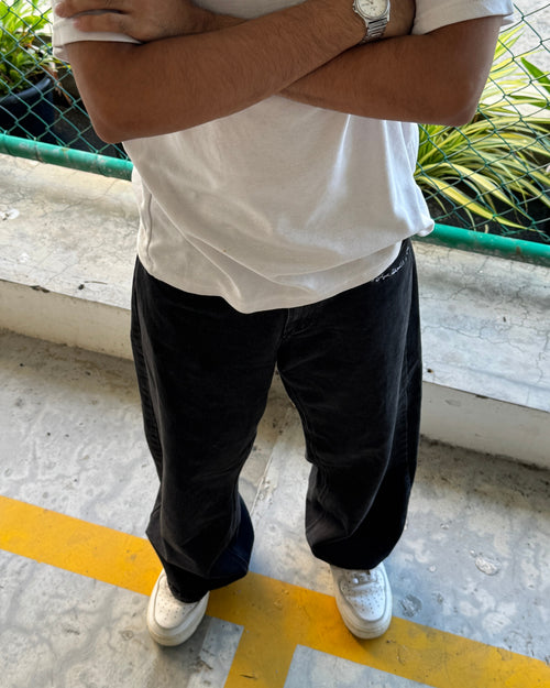 Person wearing a white shirt, black pants, and white sneakers standing on a concrete surface with a yellow line.