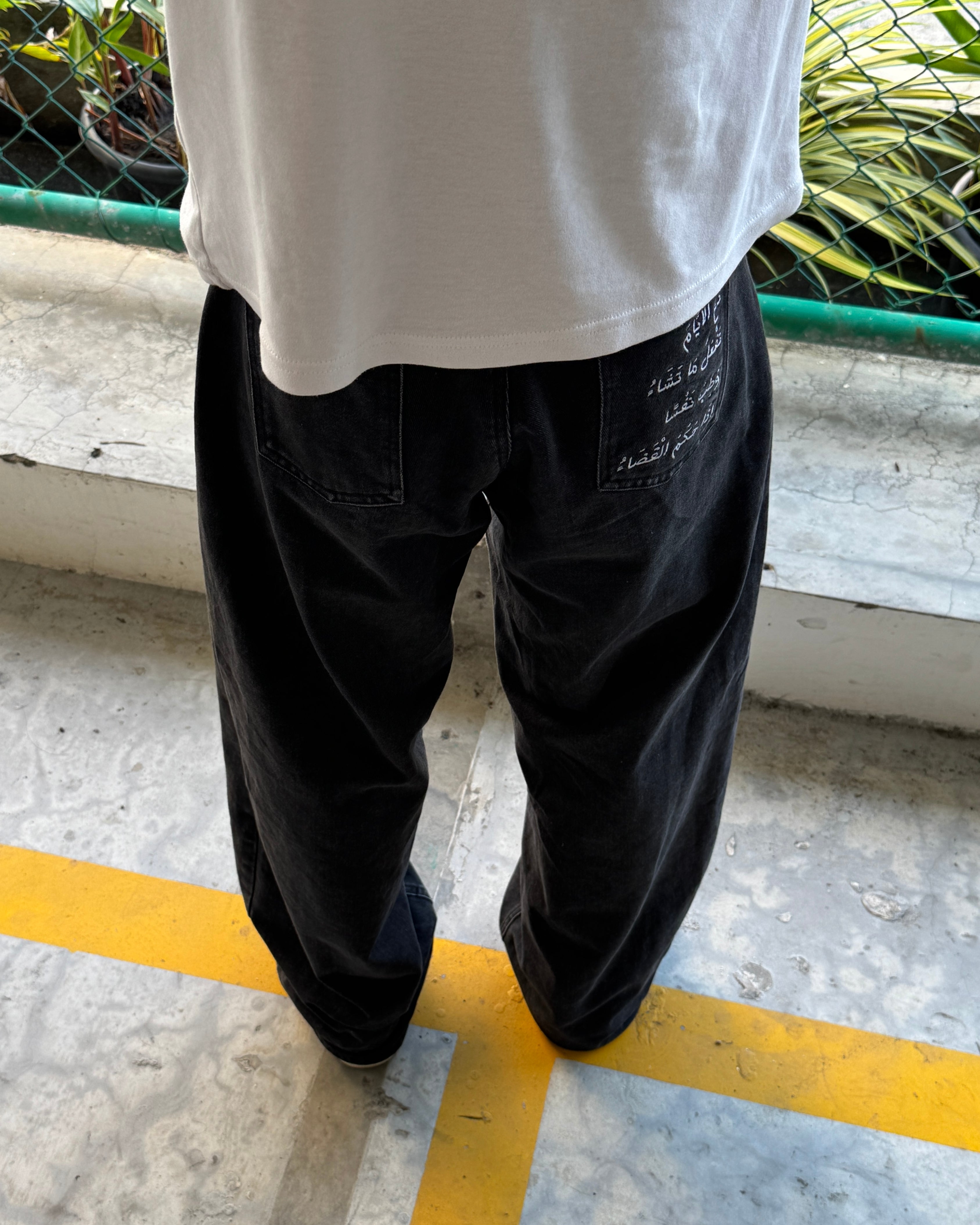Person wearing black pants and a white shirt standing on a concrete surface with a yellow line.