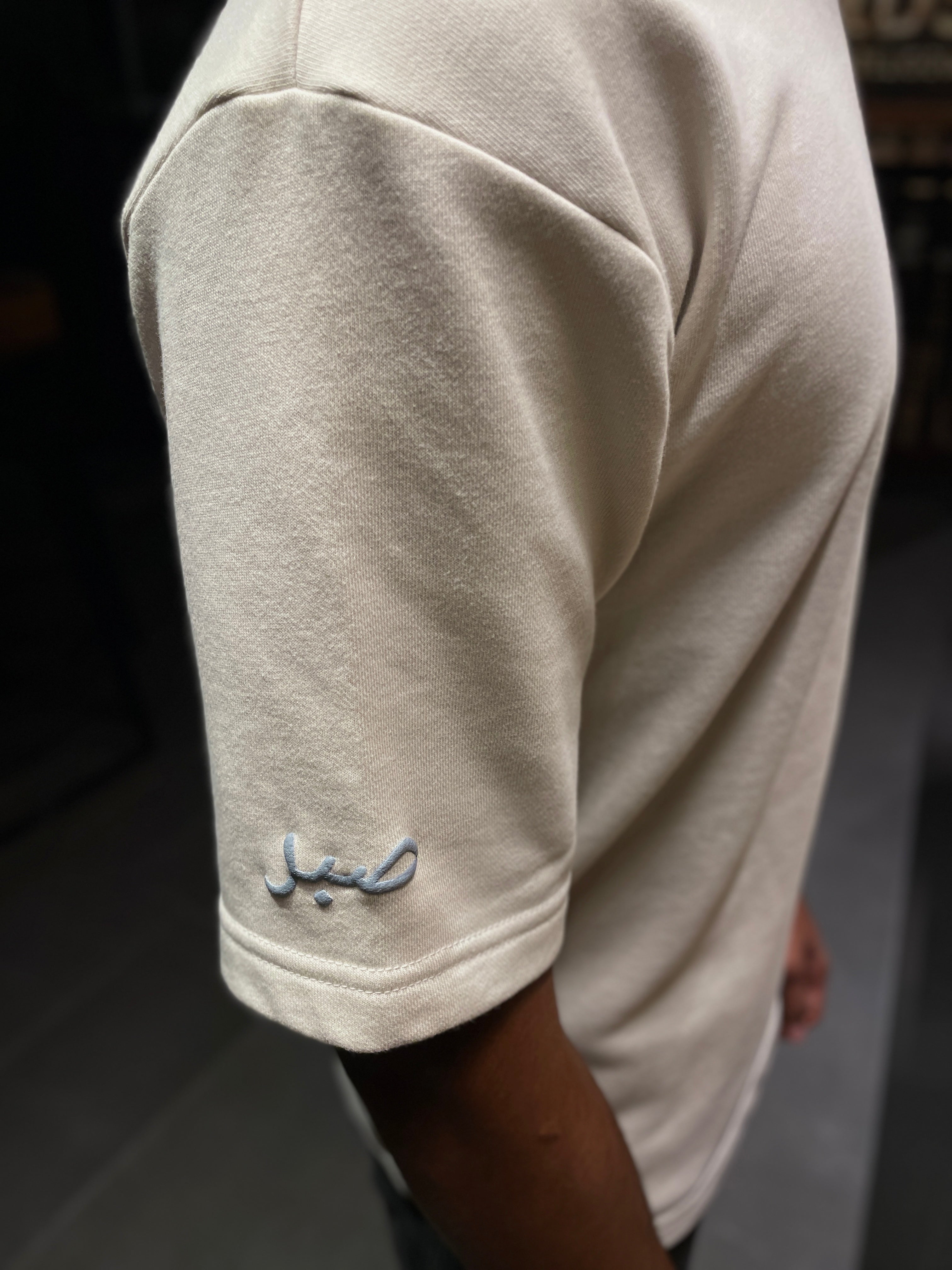 Close-up of a light beige t-shirt with a small logo on the sleeve.