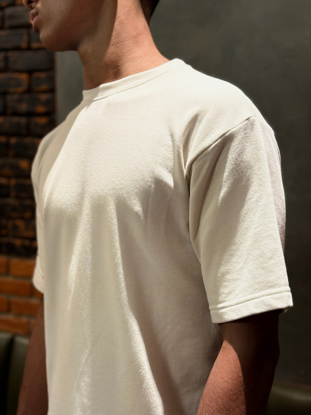 Person wearing a plain beige t-shirt against a dark background