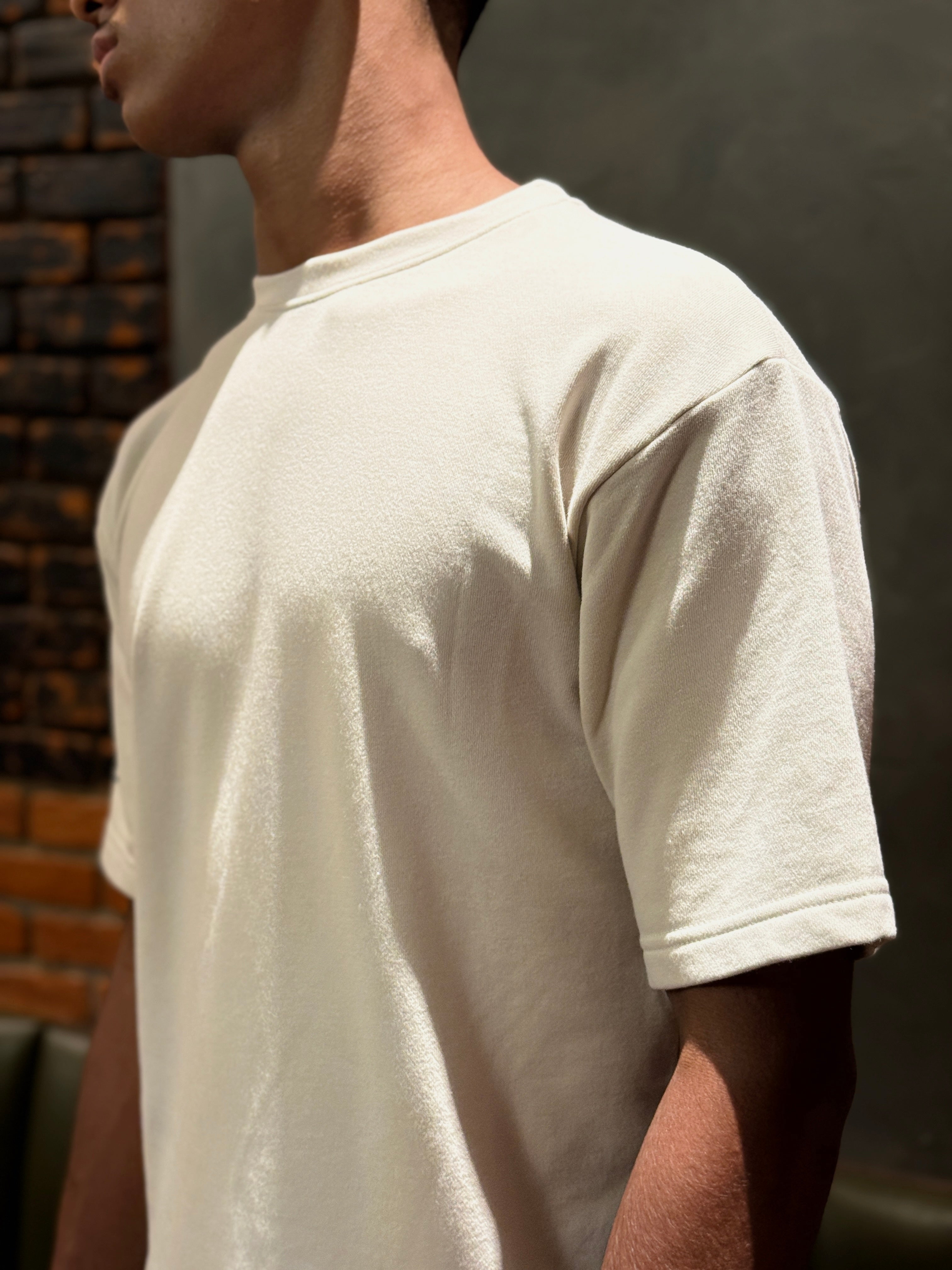 Person wearing a plain beige t-shirt against a dark background