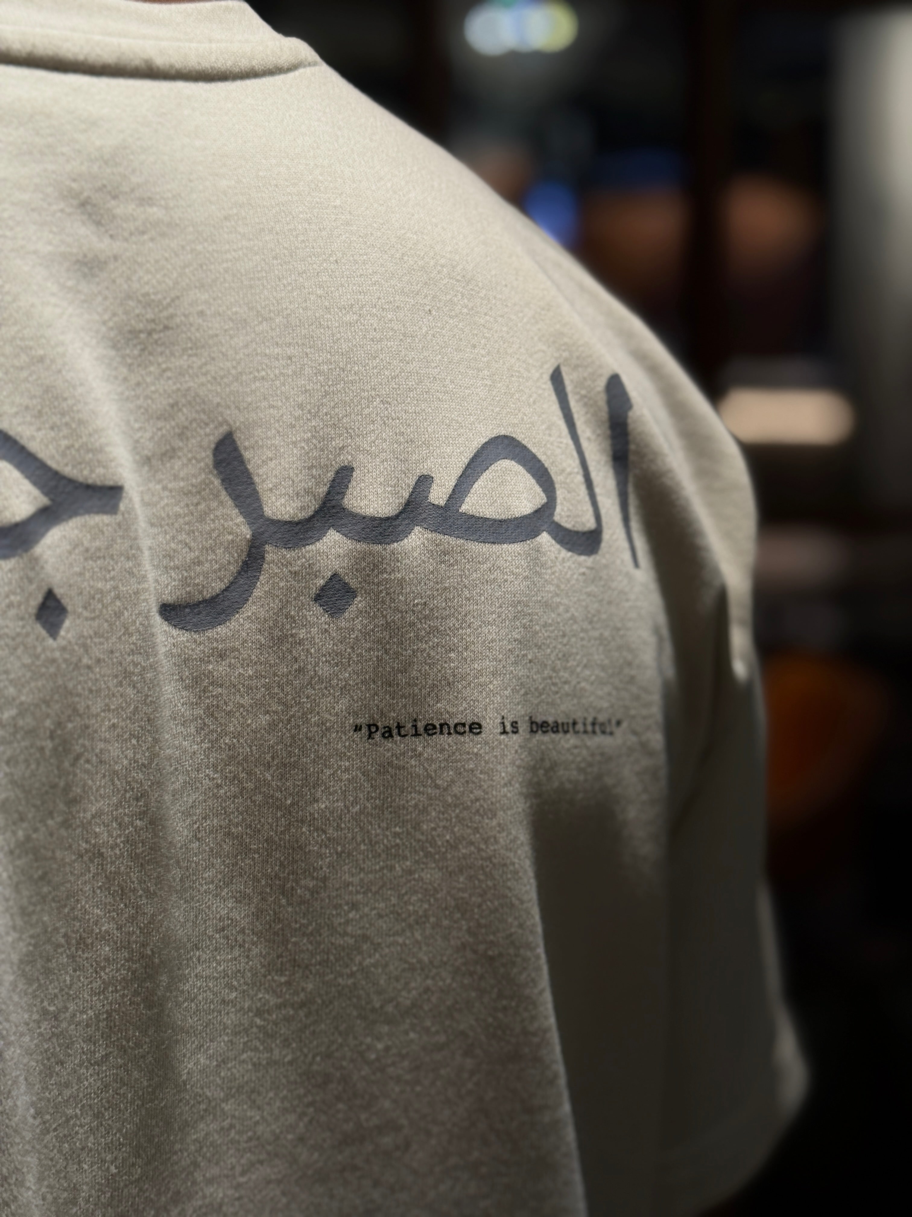 beige Tee with Arabic text and 'Patience is beautiful' on a blurred background