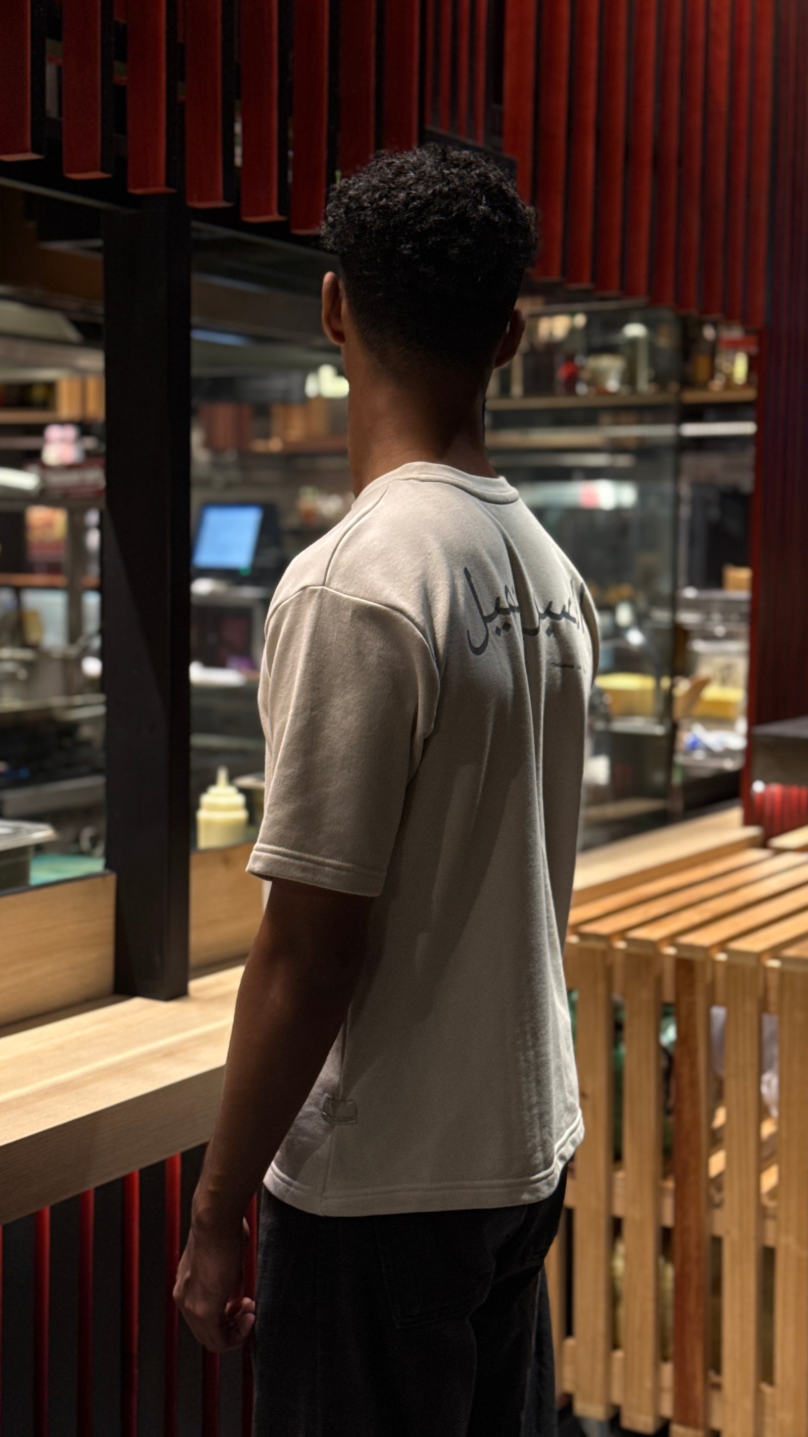 Person wearing a white t-shirt with text, standing in a modern interior setting.